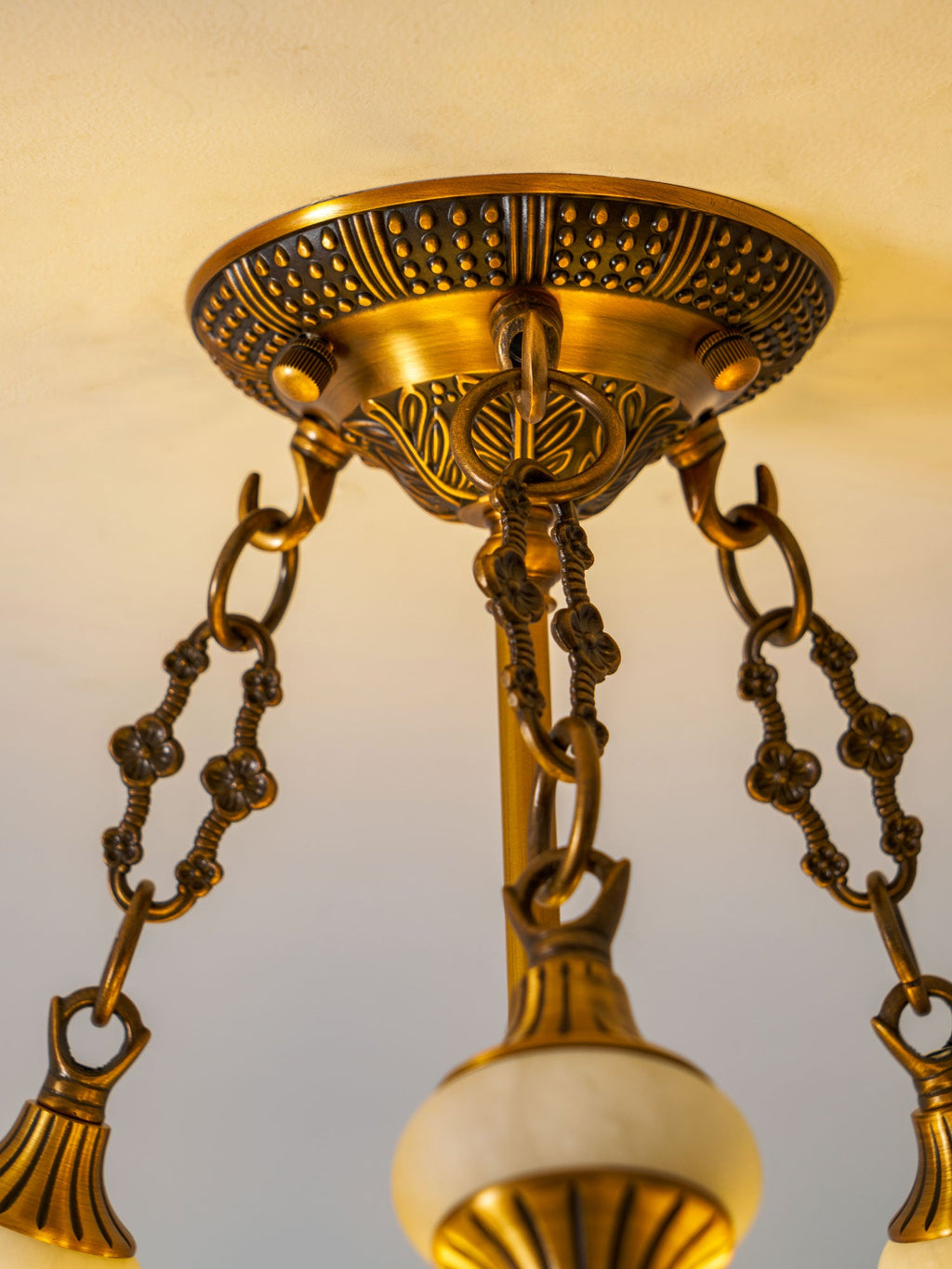 Upward close view of the cast brass canopy and chain links that carry this Clérachic ceiling light.