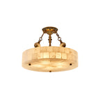 Smaller Clérachic alabaster drum ceiling light with antique brass chains, cut out on a white backdrop and lit from within.