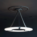 Clérachic halo pendant hung below an ornate ceiling rose in a dark panelled room.