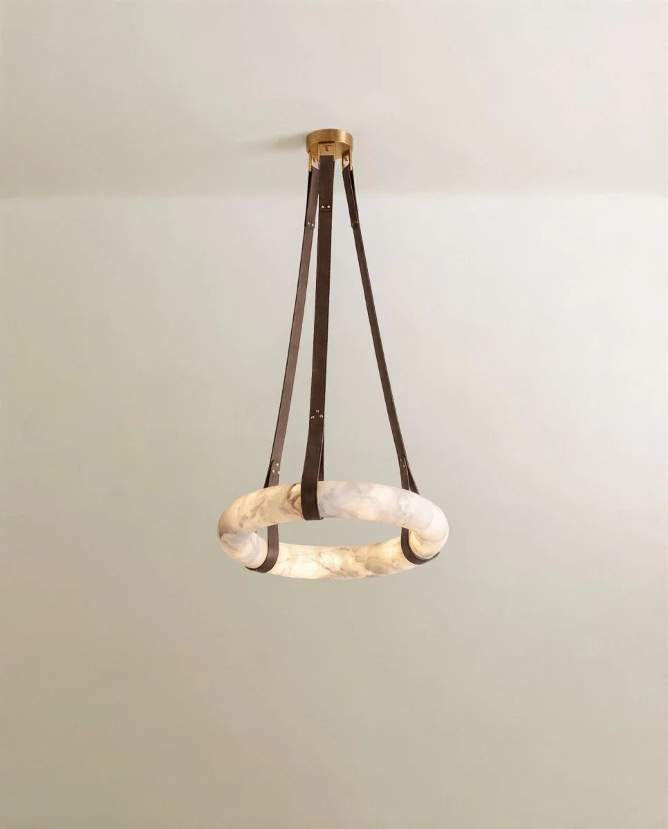 Clérachic alabaster ring pendant hung from three dark brown leather straps and a gold canopy, lit against a pale wall.