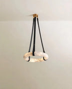 Clérachic alabaster ring pendant on three black leather straps with a gold canopy, the stone glowing against a pale wall.
