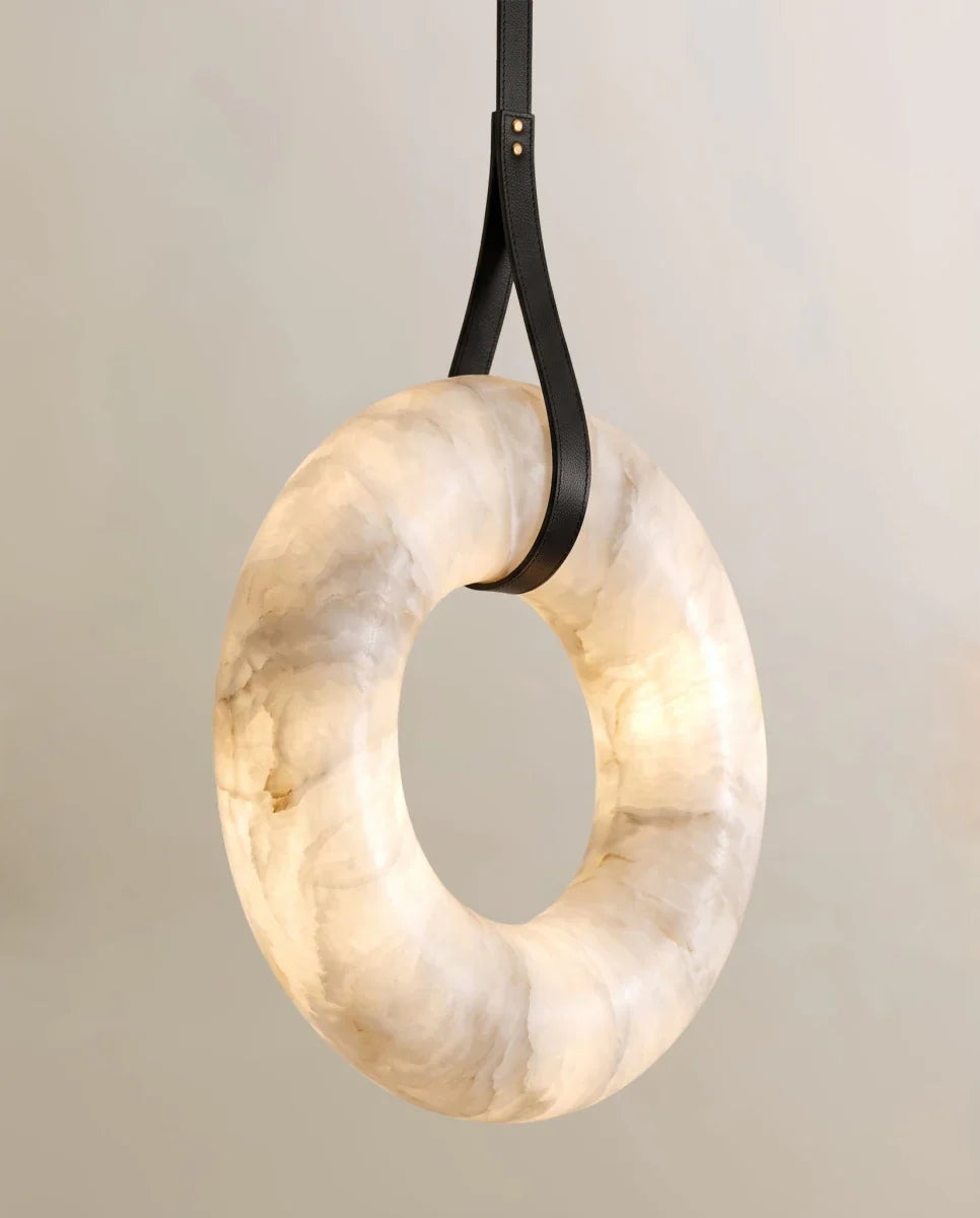 Close view of the Clérachic alabaster ring looped by a black leather strap with two gold rivets, the veining lit from inside.
