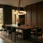 Clérachic alabaster ring pendant on tan leather straps lighting a long walnut dining table in a dark panelled room.