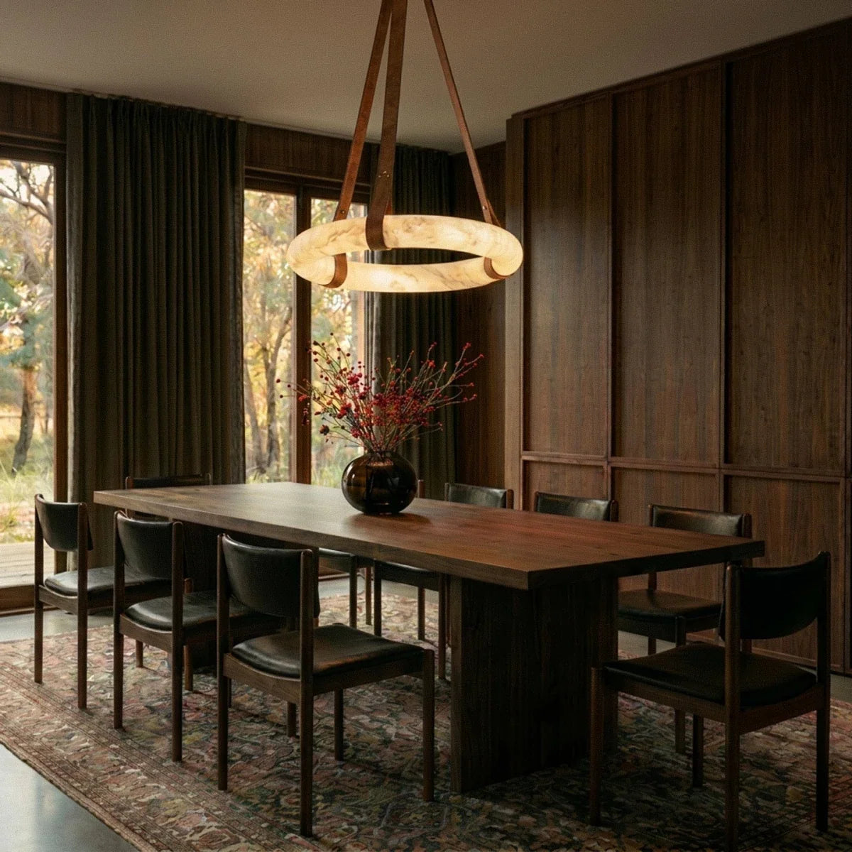 Clérachic alabaster ring pendant on tan leather straps lighting a long walnut dining table in a dark panelled room.