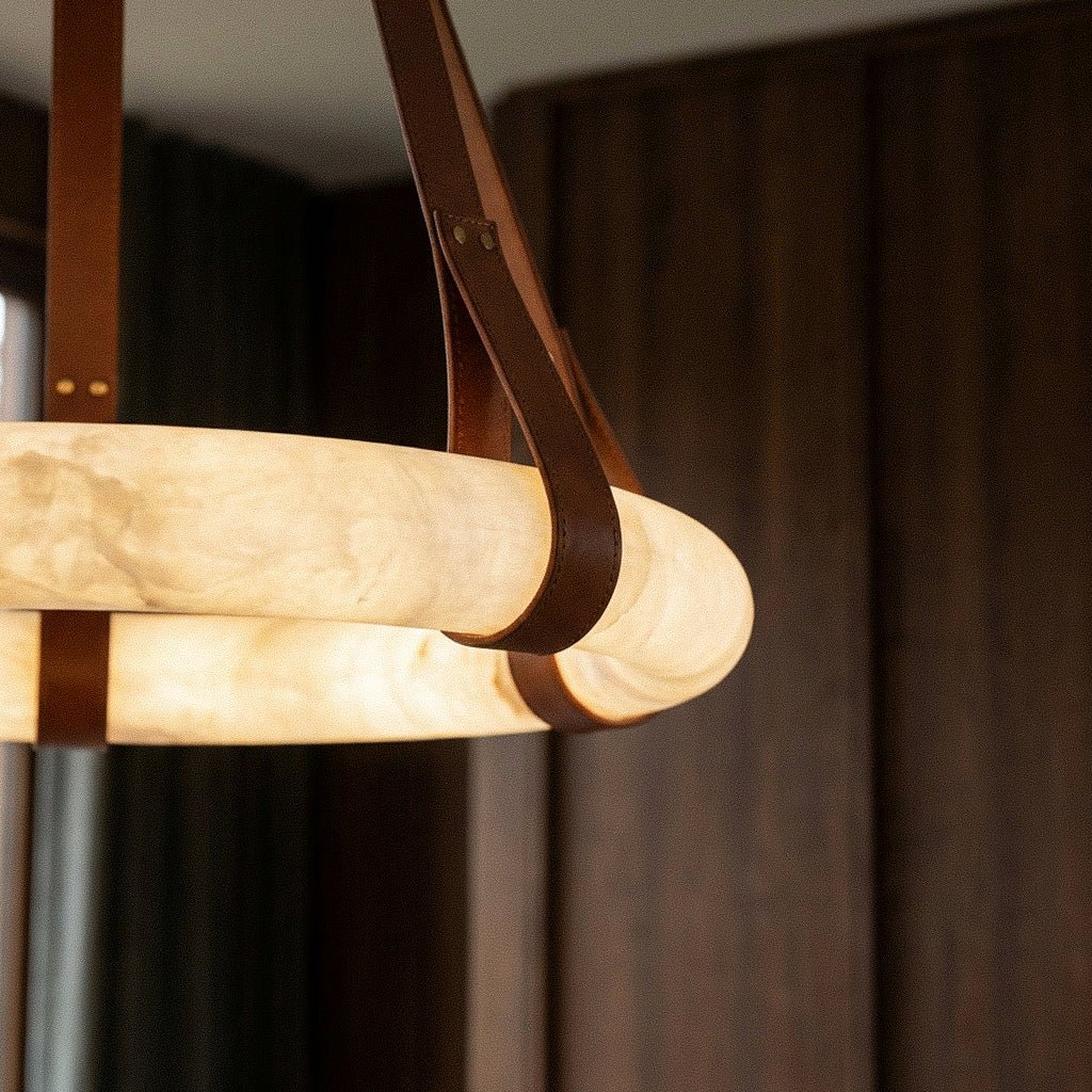 Close view of the glowing Clérachic alabaster ring with a looped tan leather strap, set against dark walnut panelling.
