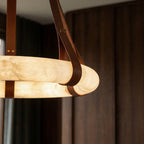 Close view of the glowing Clérachic alabaster ring with a looped tan leather strap, set against dark walnut panelling.