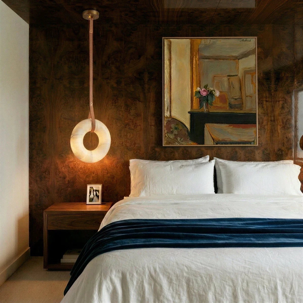Clérachic single-strap alabaster ring pendant glowing beside a bed, in front of a burr walnut panelled wall.