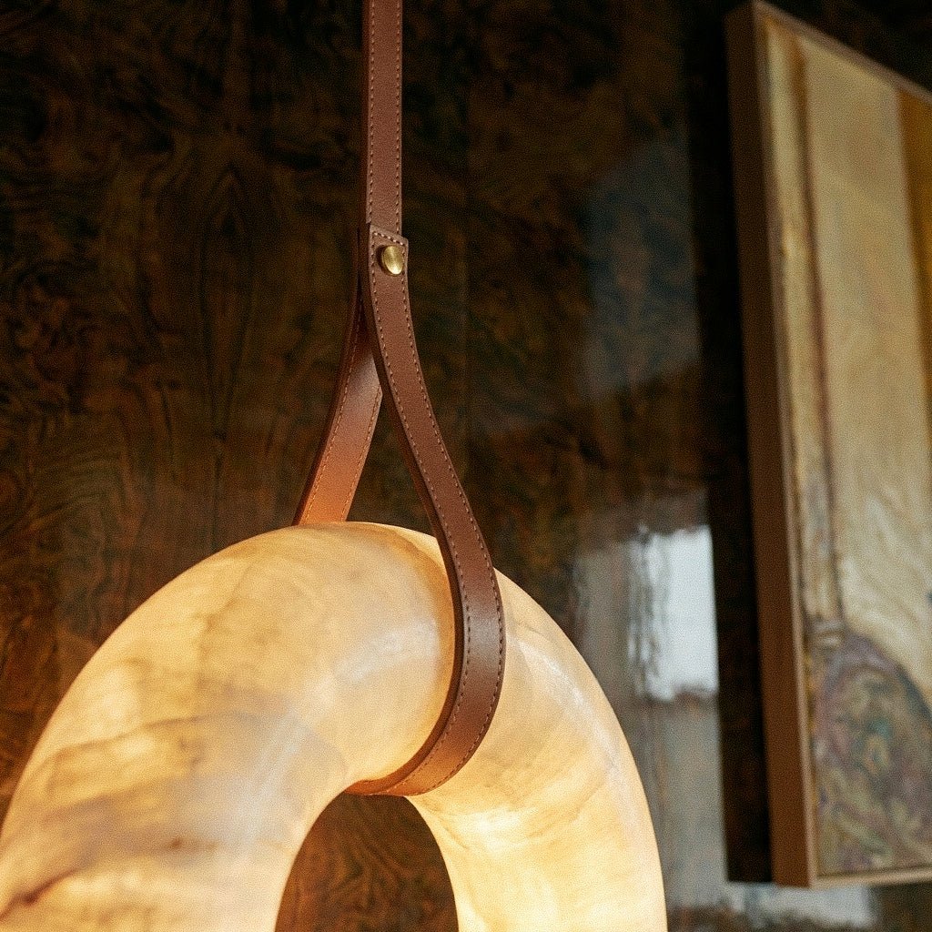 Clérachic tan leather strap with a gold stud looping over the glowing alabaster ring, beside a framed painting.