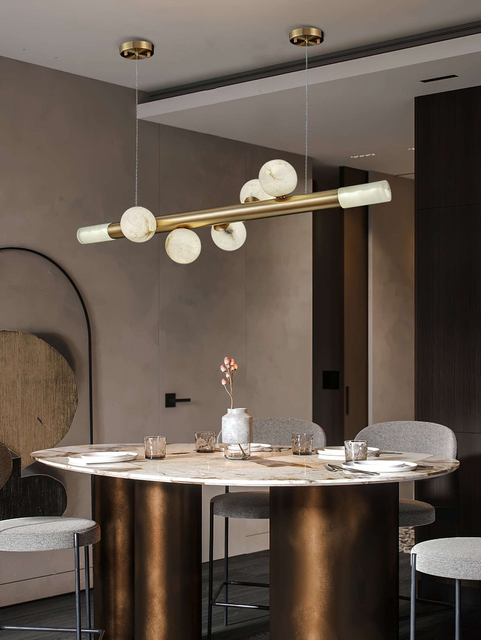 Clérachic Alabaster Linear Bar Pendant Light lit over a round marble dining table in a taupe room with an arched mirror.