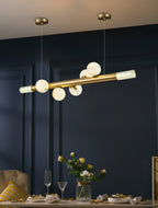 Clérachic Alabaster Linear Bar Pendant Light against deep navy panelling, its stones glowing over a table set with yellow roses.