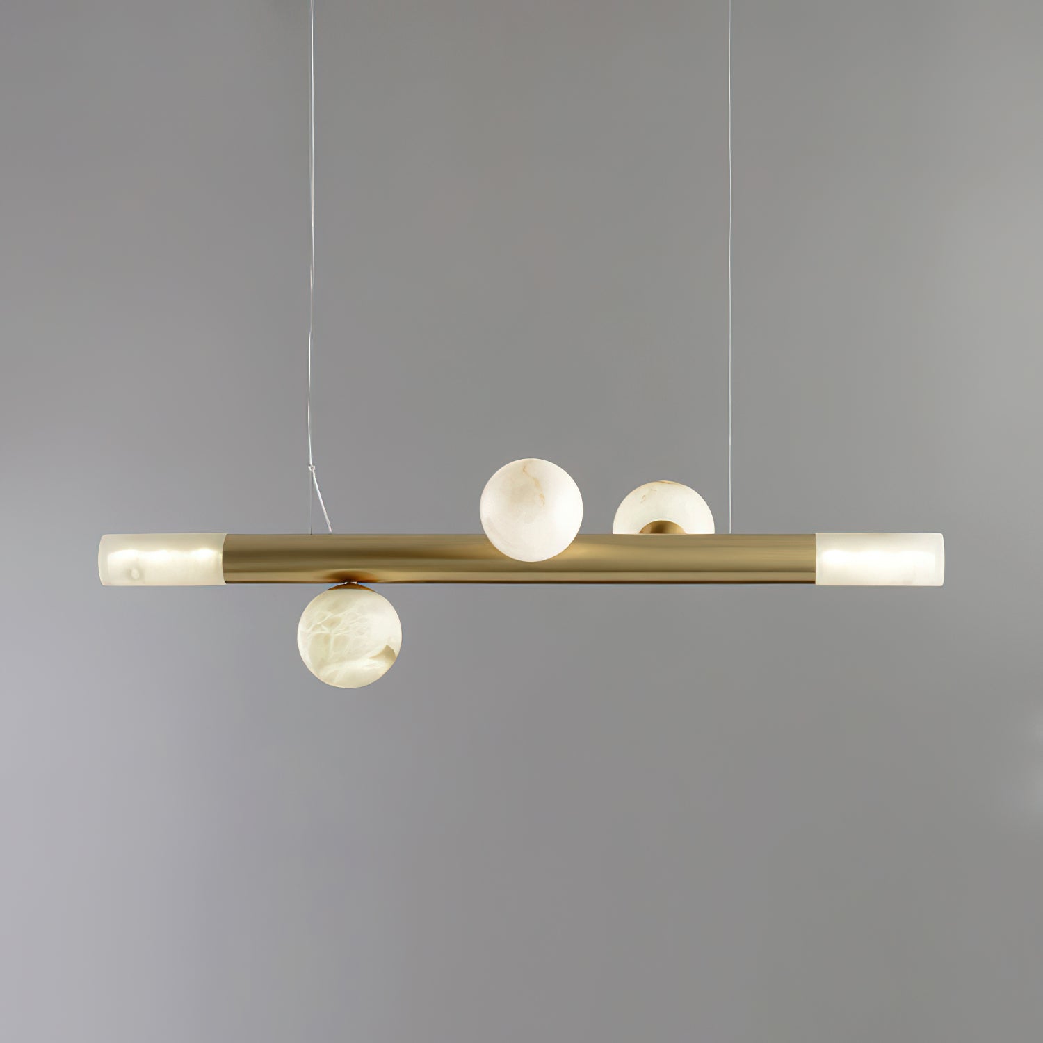 Three-globe Clérachic Alabaster Linear Bar Pendant Light on a soft grey backdrop, two stones above the bar and one below.