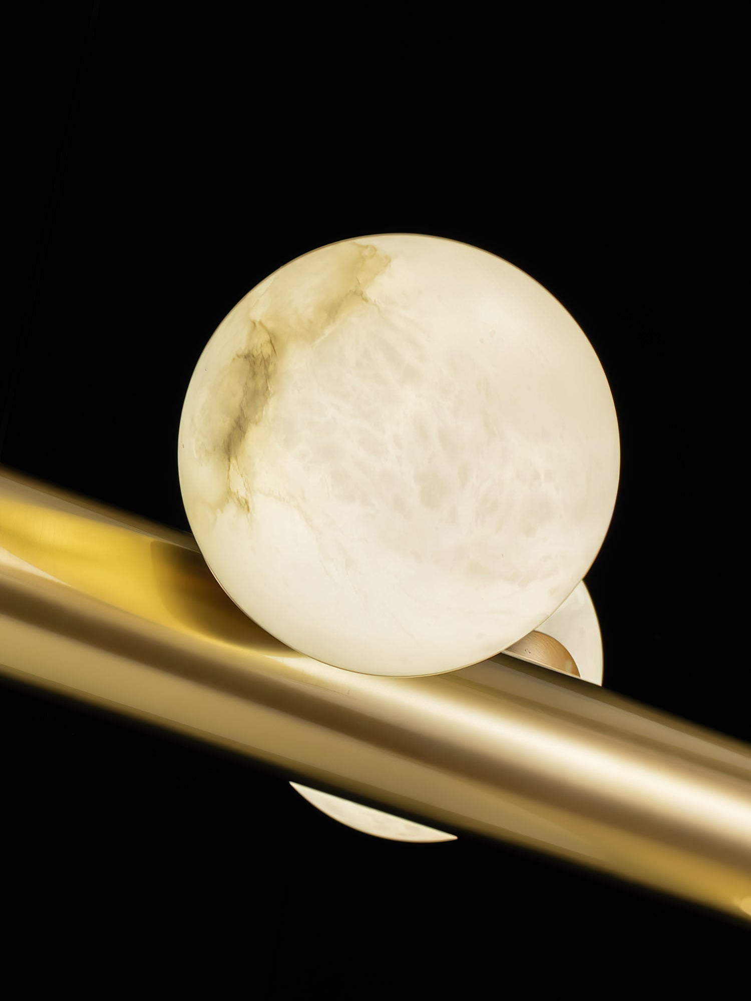 Close-up of one alabaster globe on the Clérachic Alabaster Linear Bar Pendant Light, seated against the polished brass tube.