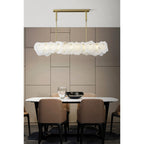 Clérachic alabaster linear chandelier lit above a marble dining table with tan leather chairs and a panelled taupe wall