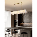 Clérachic alabaster linear chandelier over a stone kitchen island with black stools and a grey marble splashback