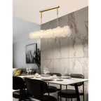 Clérachic alabaster linear chandelier above a laid dining table, wine glasses and plates set against a marble tile wall