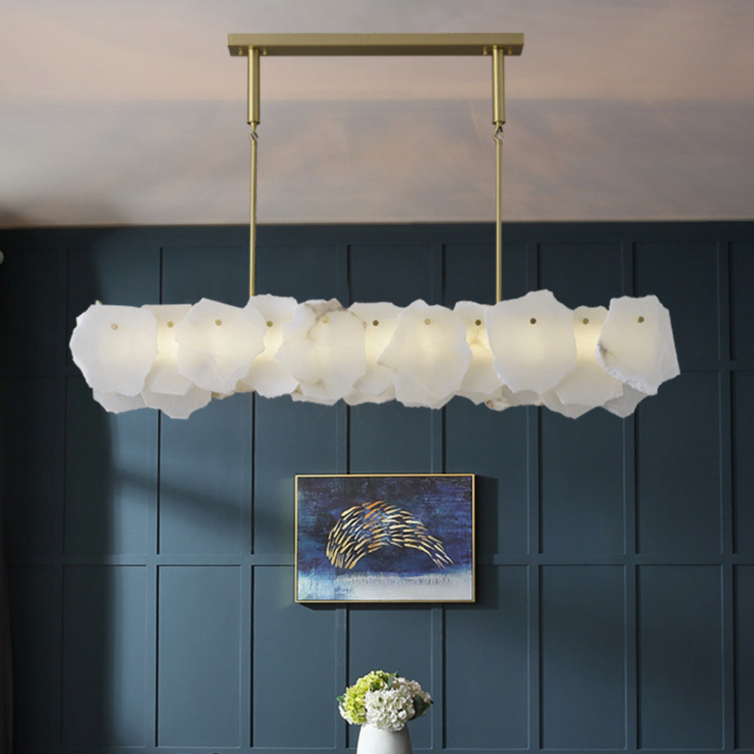 Clérachic alabaster linear chandelier lit against a navy panelled wall with framed art and white hydrangeas below