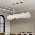 Clérachic alabaster linear chandelier above a round dining table beside an arched window of fluted glass