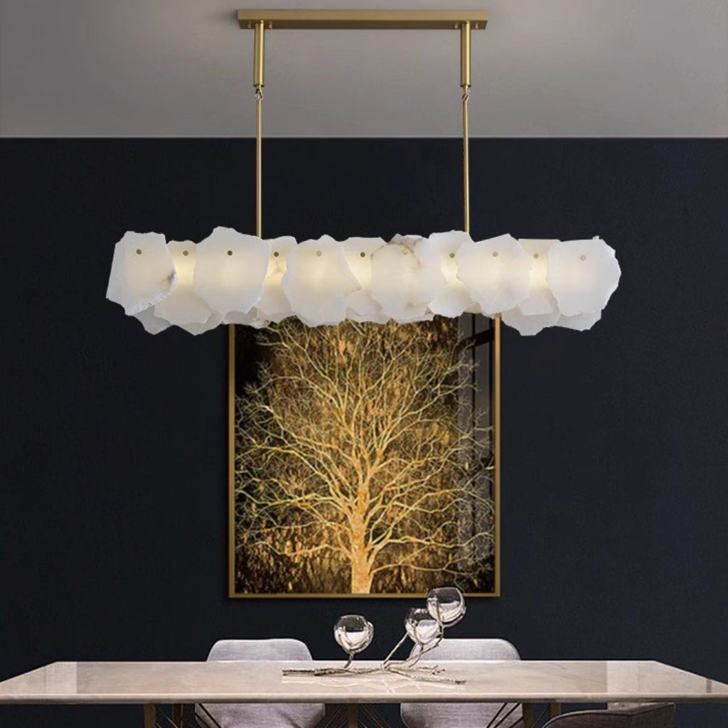 Clérachic alabaster linear chandelier lit against a dark wall hung with a gilded tree canvas above a stone table