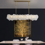 Clérachic alabaster linear chandelier lit against a dark wall hung with a gilded tree canvas above a stone table