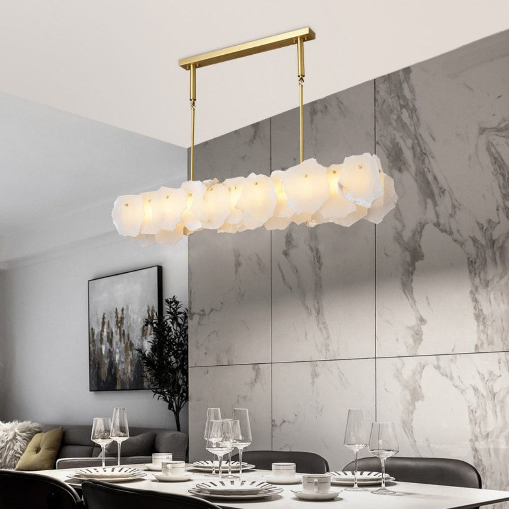 Clérachic alabaster linear chandelier over a set dinner table, a marble wall behind and a sofa in the far corner