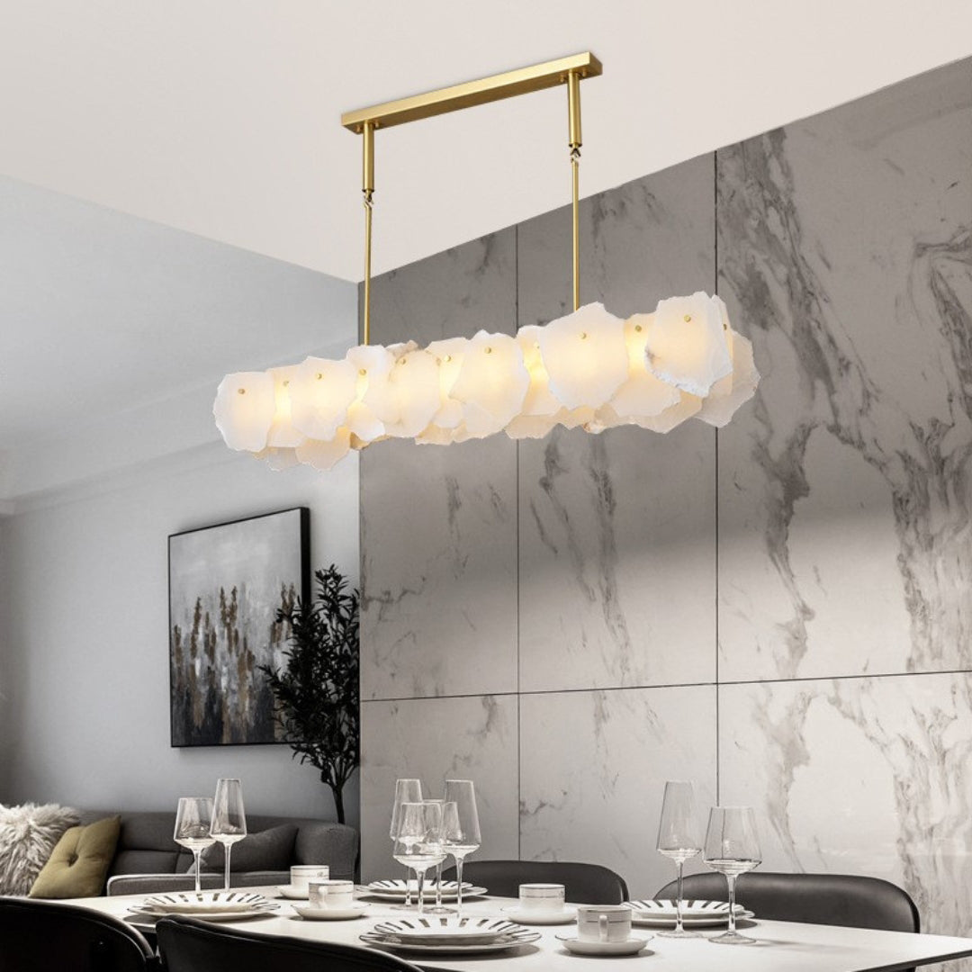 Clérachic alabaster linear chandelier over a set dinner table, a marble wall behind and a sofa in the far corner