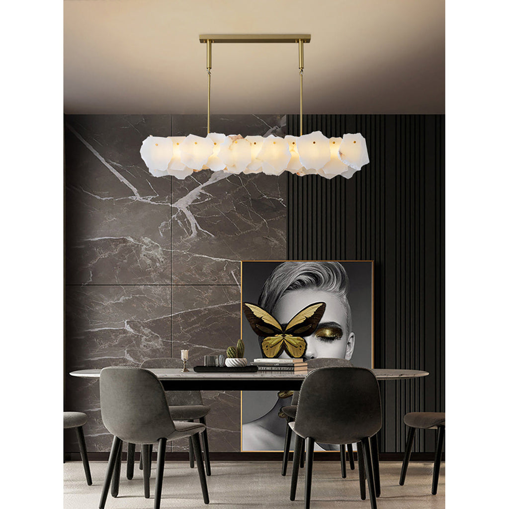 Clérachic alabaster linear chandelier above an oval dining table against brown marble and dark slatted panelling