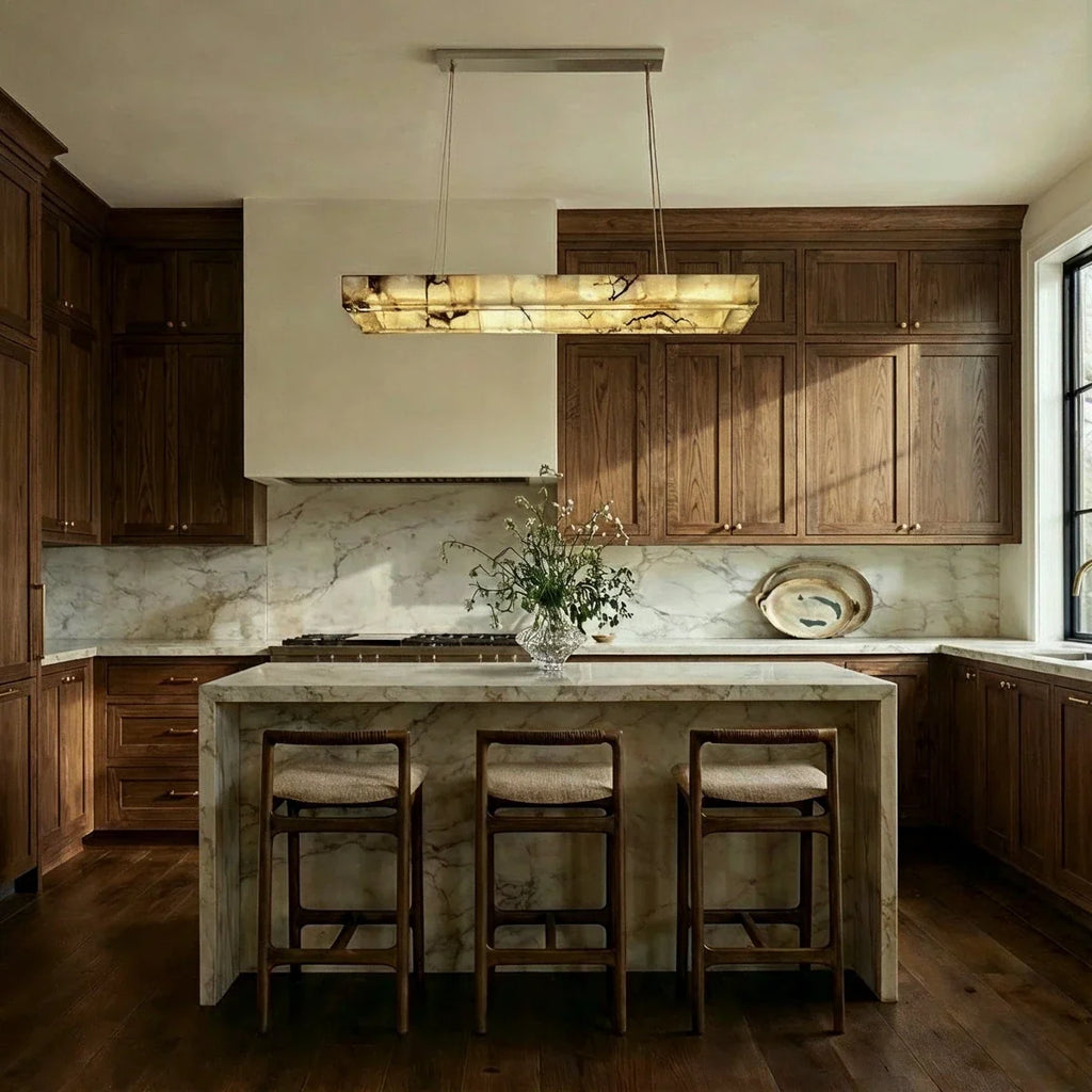 Clérachic rectangular alabaster chandelier above a marble kitchen island with three woven-seat stools.