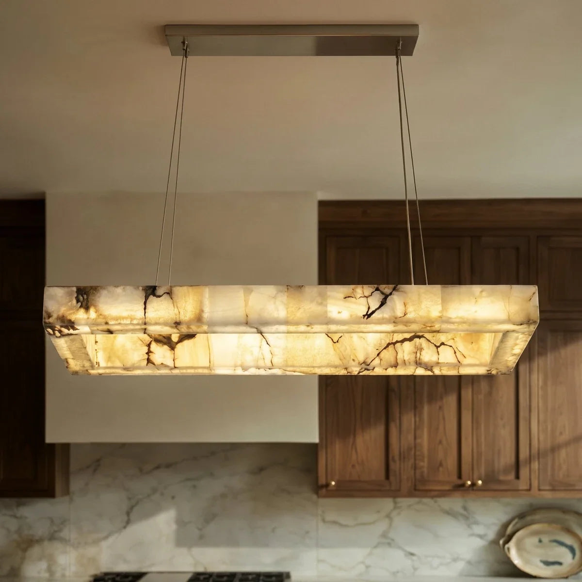 Clérachic alabaster chandelier in a kitchen, its stone shade lit warm beneath a brushed metal canopy.