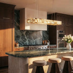 Clérachic rectangular alabaster chandelier above a dark green stone kitchen island with leather-topped stools.