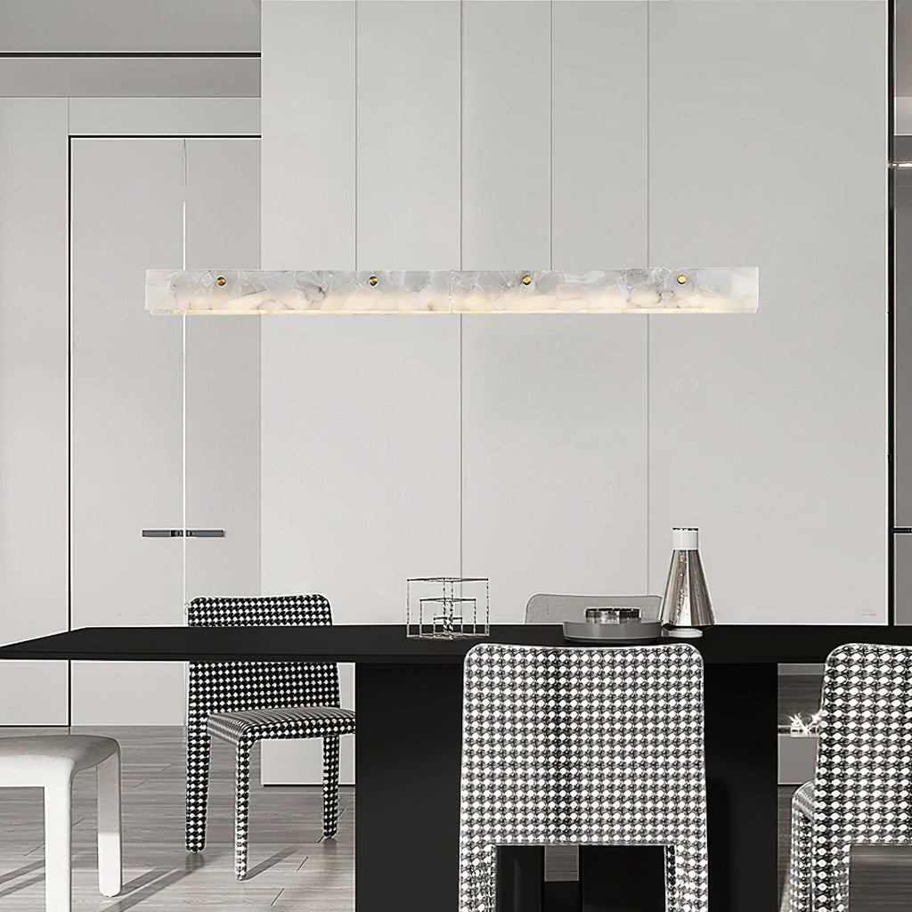 Clérachic alabaster pendant over a black dining table, warm light picking out houndstooth chairs in a pale open-plan room.