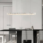 Clérachic alabaster pendant over a black dining table, warm light picking out houndstooth chairs in a pale open-plan room.