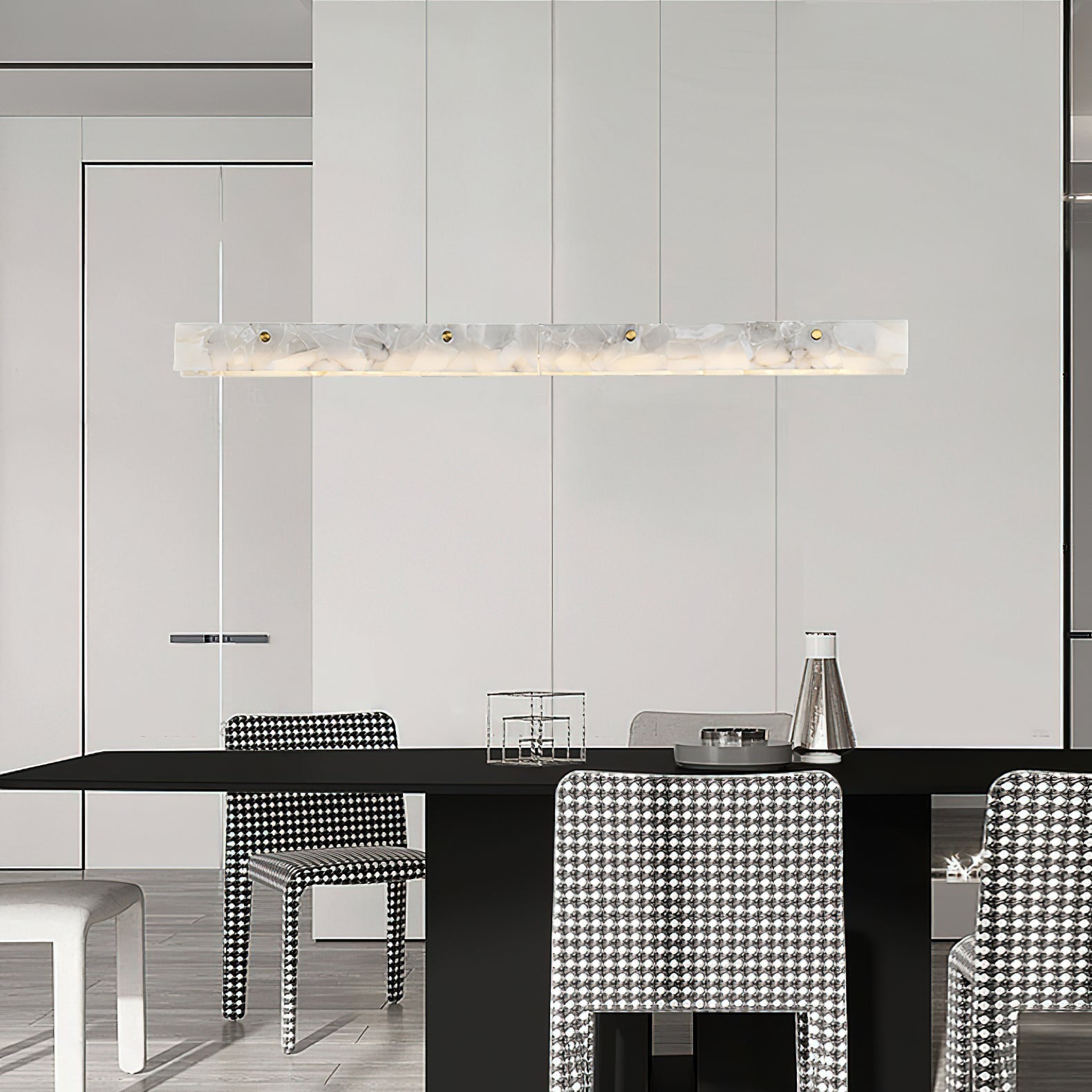 Clérachic alabaster pendant over a black dining table, warm light picking out houndstooth chairs in a pale open-plan room.