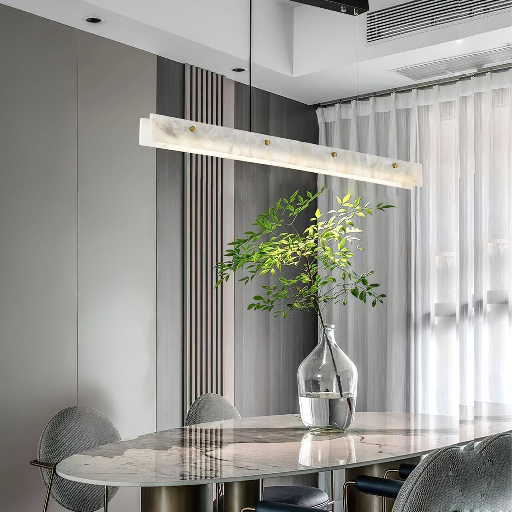 The Clérachic linear light above a round marble table, sheer curtains behind and an olive branch in a glass vase alongside.