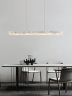 Clérachic pendant hung over a slim white dining table, its stone bar echoing the pale plaster wall behind.