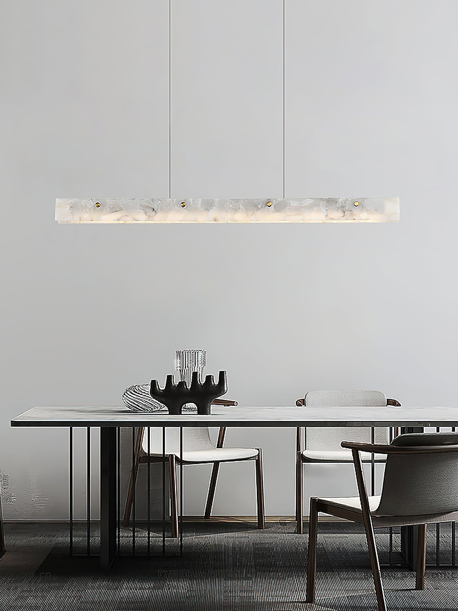 Clérachic pendant hung over a slim white dining table, its stone bar echoing the pale plaster wall behind.