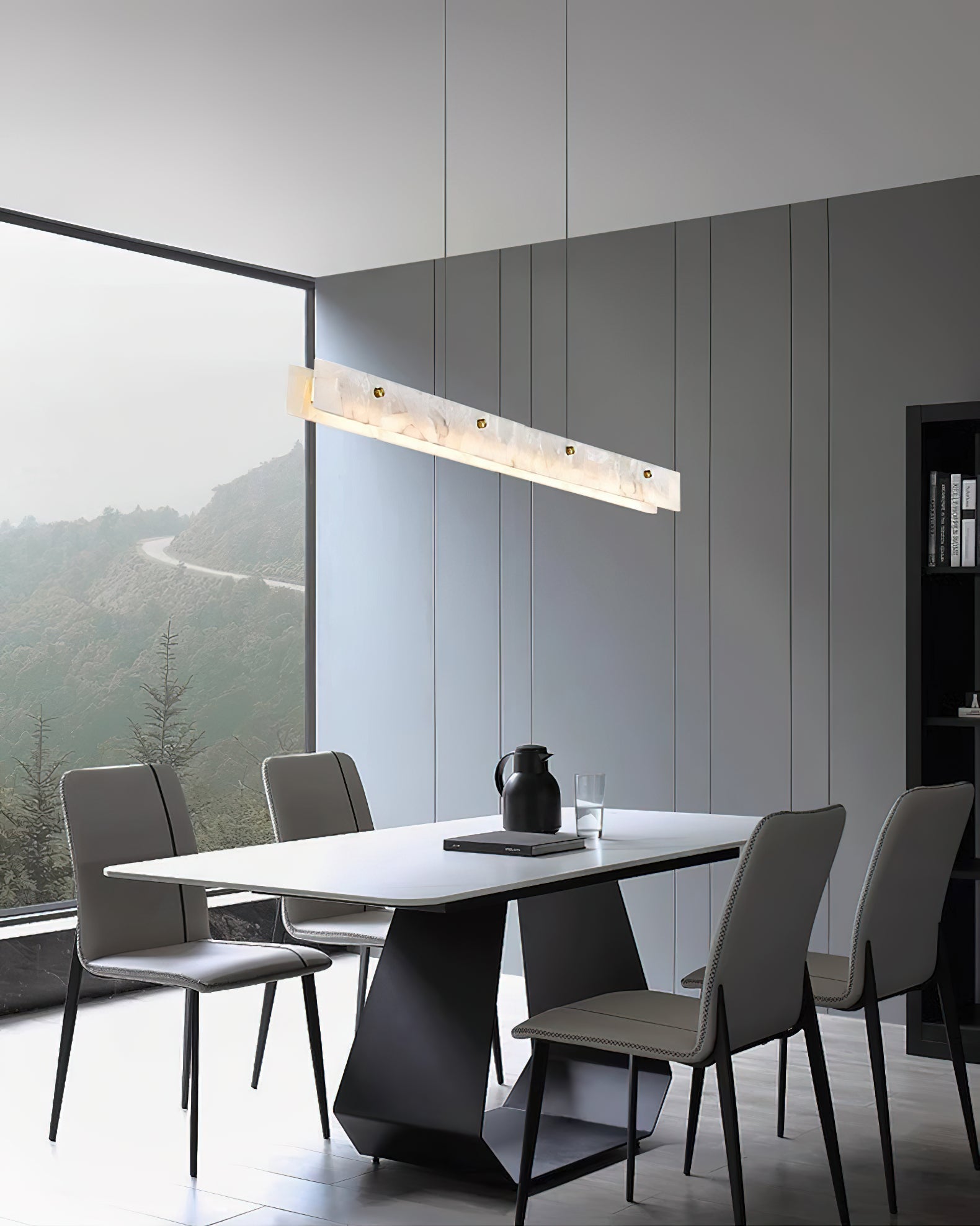 The Clérachic fixture lit above a dining table set against a window framing misty hills.