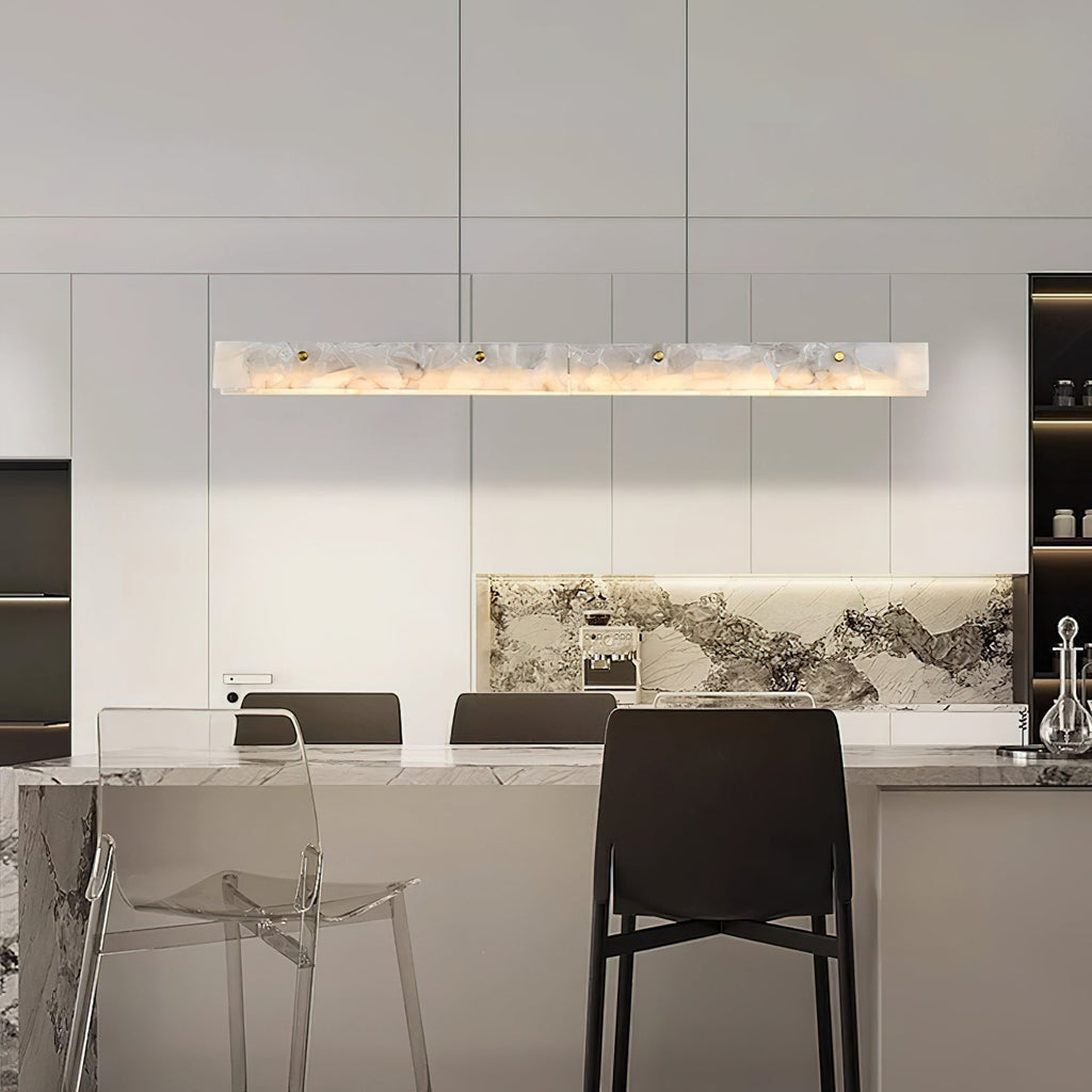 The Clérachic linear light above a kitchen island, warm glow against a veined marble splashback and bar stools.