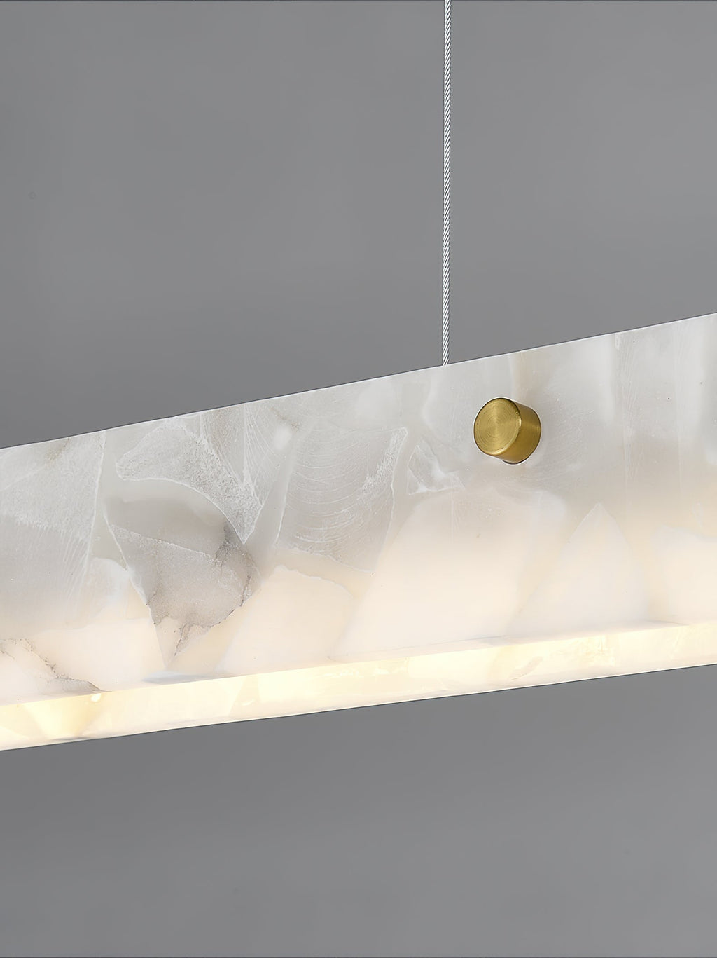 The Clérachic diffuser in close-up, a brushed brass stud set into the cloudy alabaster with light spilling from the lower edge.