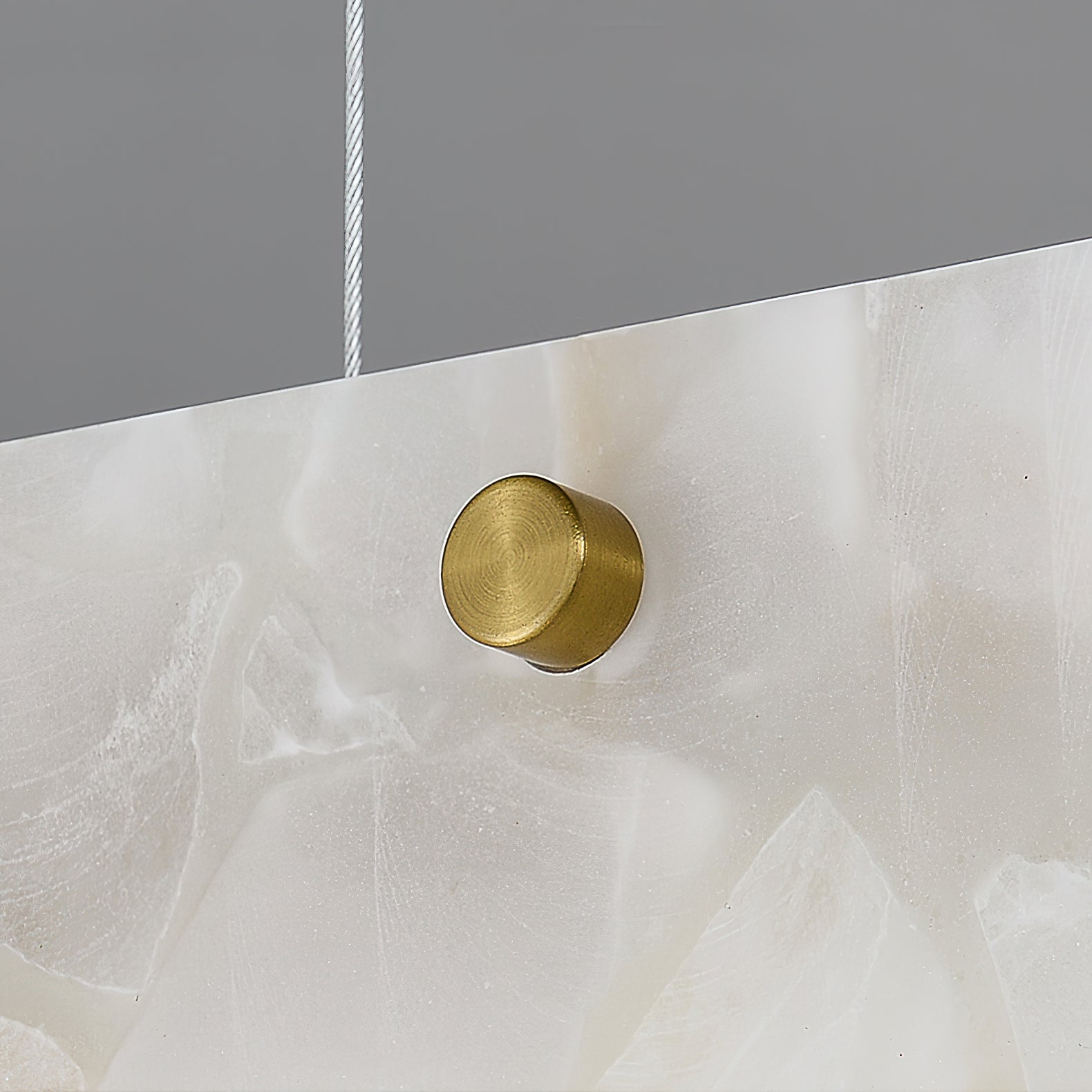 Clérachic brass stud shown in macro against the alabaster face, with the fine steel suspension cable rising above it.