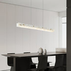 The Clérachic fixture angled above a black dining table, its glow raking a white panelled wall.