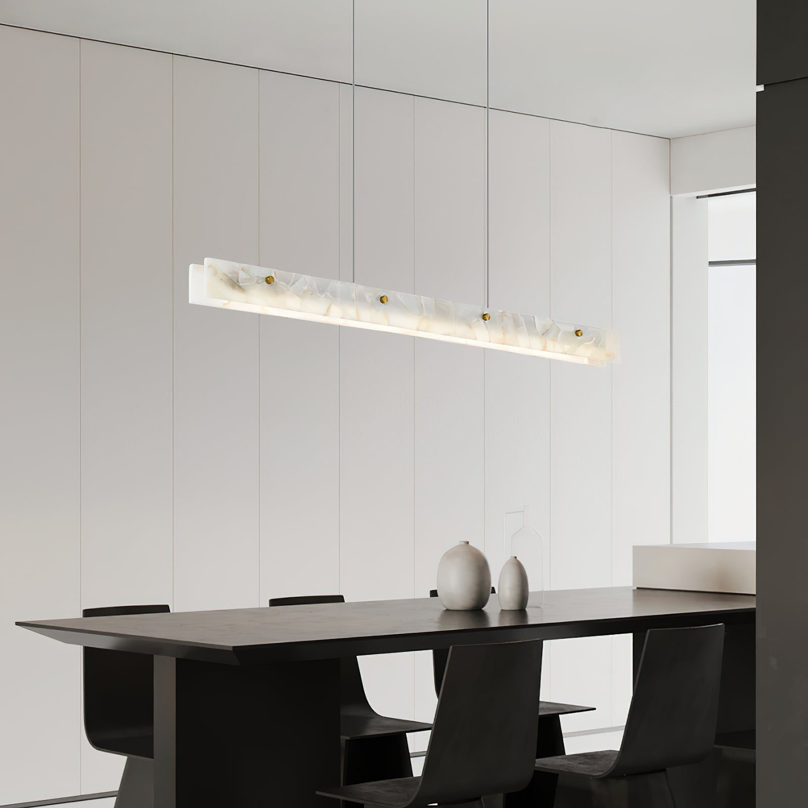The Clérachic fixture angled above a black dining table, its glow raking a white panelled wall.