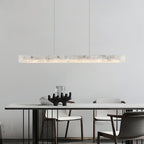 Clérachic alabaster pendant lit above a white dining table with dark timber chairs in a calm, pale room.