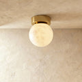 Clérachic round alabaster globe ceiling light, softly lit, with cloudy veining and a round brushed brass canopy.
