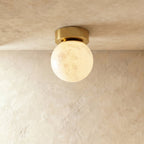 Clérachic round alabaster globe ceiling light, softly lit, with cloudy veining and a round brushed brass canopy.