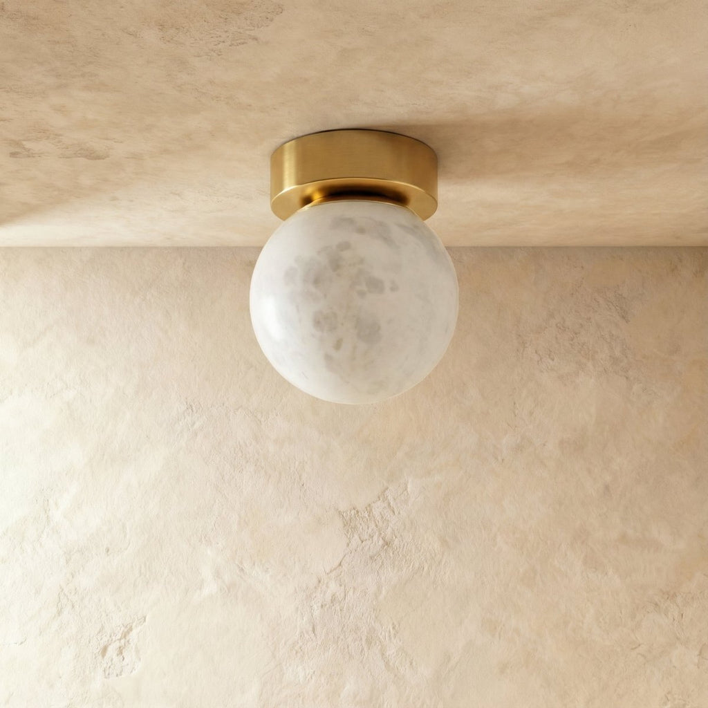 Clérachic round alabaster globe ceiling light unlit, pale grey-white stone with soft veining on a brass canopy.