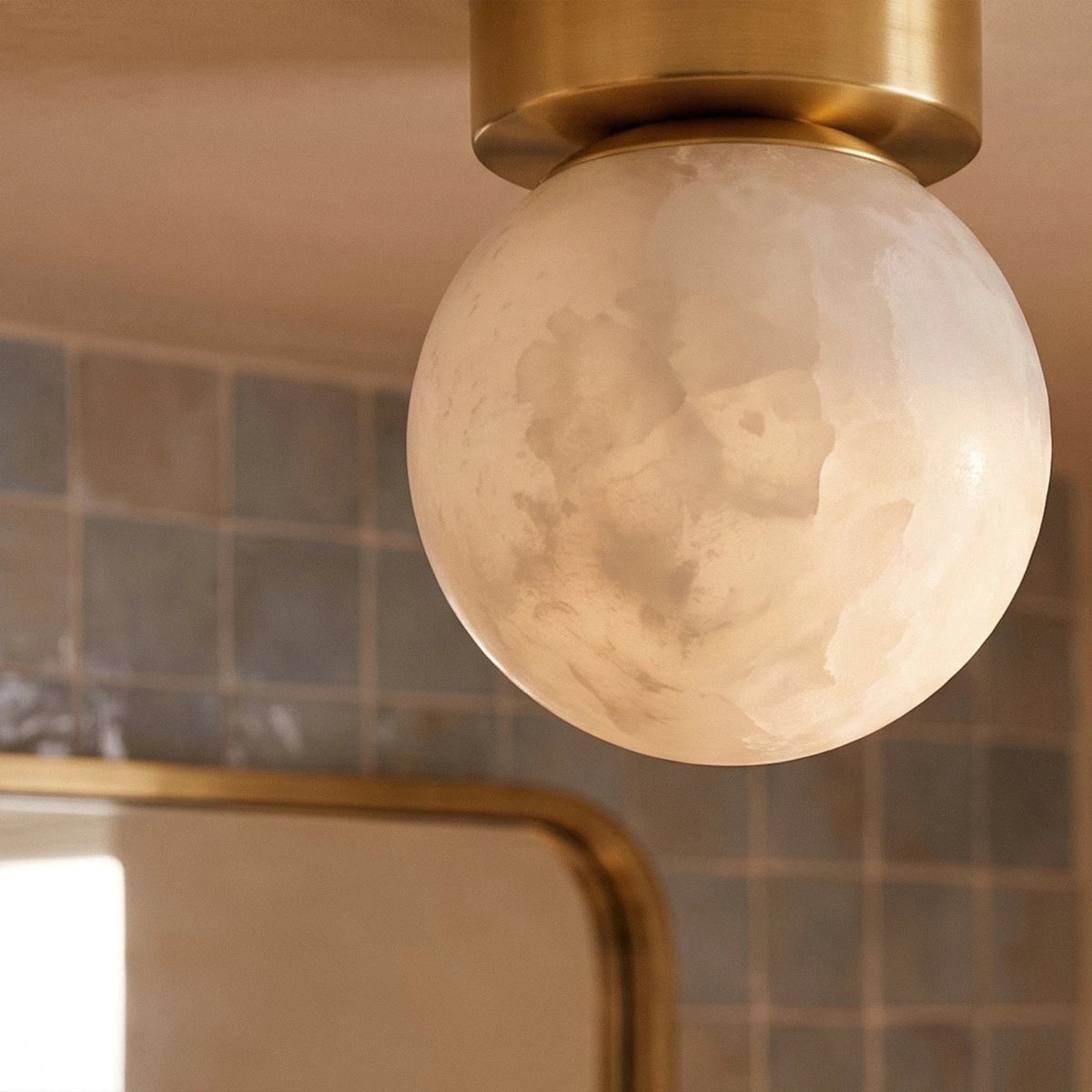Clérachic close-up of the lit alabaster globe, showing cloudy cream veining and the brushed brass canopy above it.