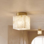 Clérachic close-up of the lit square alabaster ceiling light, bold cream veining and a brushed brass canopy, a second light behind.