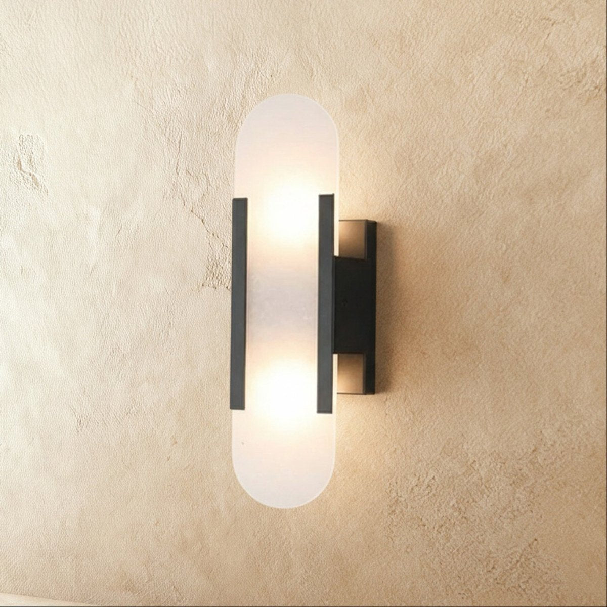 Clérachic wall light with a frosted pill-shaped alabaster shade, black metal bars and a black wall plate.