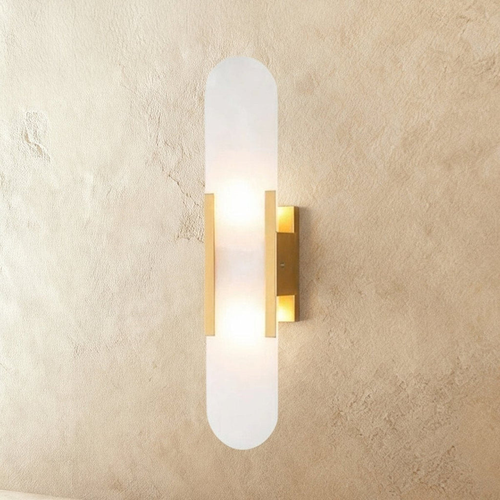 Clérachic tall wall light: a slim pill-shaped alabaster shade on gold bars, lit by two bulbs behind it.