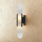 Clérachic tall wall light with a veined alabaster shade, black bars and a black wall plate, softly lit.